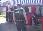 Funkcjonariusz Służby Celno-Skarbowej stoi przed straganem z podrobioną odzieżą (koszulki, spodnie, spodnie dresowe).